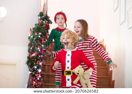 Kids running stairs on Christmas morning. Children in pajamas run downstairs eager to open Xmas presents. Celebration at home. Winter family holiday. Boy and girl opening gifts.