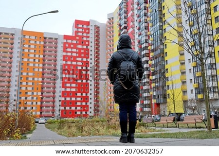 New residential district in autumn city, woman in black leather coat standing on apartment building background. Real estate, choosing home or renting property concept Royalty-Free Stock Photo #2070632357