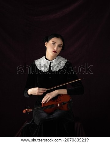 Portrait of an young beautiful caucasian woman holding a violin on the black background