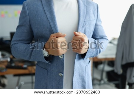 Close-up of businessman wearing stylish costume and corrects jacket with hand. Well-dressed man posing in personal office. Presentable look at work. Business and job concept Royalty-Free Stock Photo #2070652400