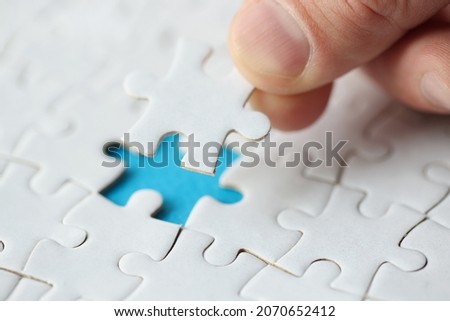 Close-up of persons hand putting last missing puzzle. Searching solution for problem. Fragment of white puzzle. Business strategy and complete mission concept