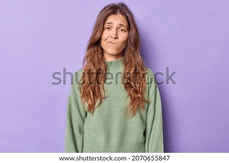 Studio shot of displeased bored woman purses lips and looks with uninterested expression wears casual jumper poses alone against purple background. Upset gloomy teenage girl tired of distance studying Royalty-Free Stock Photo #2070655847