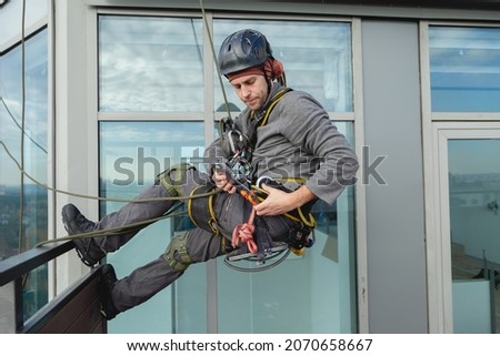 Industrial climber is preparing to hang out from the balcony of the building. Preparation for high-altitude work Royalty-Free Stock Photo #2070658667