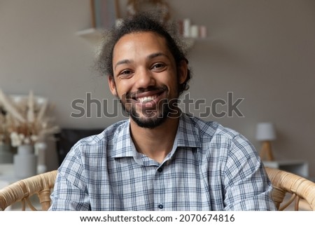 Happy millennial African American hipster guy looking at camera with toothy smile. Young business man in casual, blogger, coach, teacher giving training, making video call at home. Head shot portrait