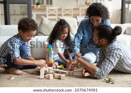 Happy millennial African family couple and little sibling kids constructing toy castle on heating floor at home, building towers from small wooden blocks, playing together, enjoying leisure, playtime Royalty-Free Stock Photo #2070674981