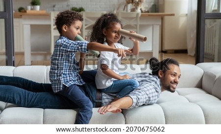 Happy African American daddy and little sibling kids playing funny active games on couch, Children sailing dad like pirate boat, holding paper toy spyglasses. Childhood, family, fatherhood
