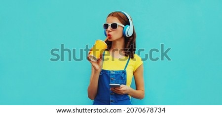 Portrait of young woman in headphones listening to music with smartphone on blue background