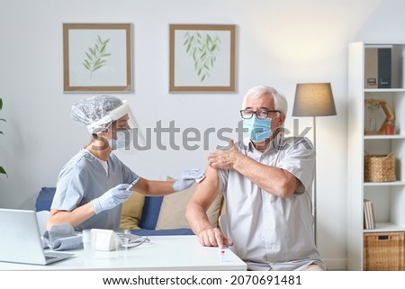 Nurse in protective mask putting the injection in the arm of senior man during his visit to hospital