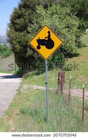 Traffic sign on a rural farmland road warning of tractors and other slow farm equipment possibly being on the road