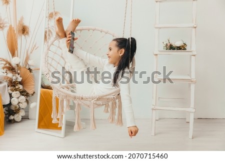 little girl is sitting and looking at her mobile phone, resting on a hanging chair.