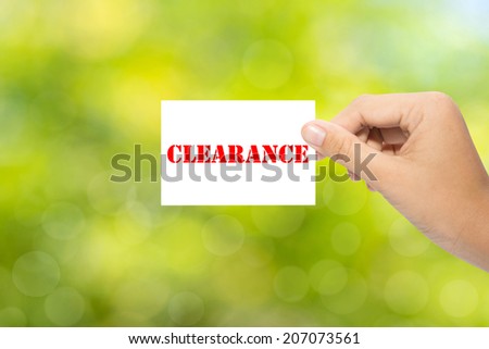 Hand holding a paper CLEARANCE on green background