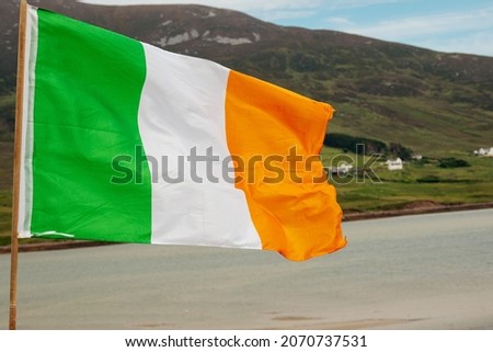 National tri color flag republic of Ireland. Green mountain and cloudy sky in the background. County Mayo.
