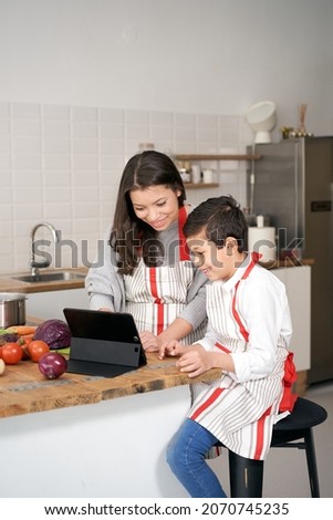 Vertical photo. In the kitchen: A single-parent family cooking. Mother and son searching for an online cooking recipe via their tablet. Children helping parents. Healthy eating.