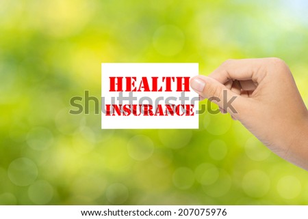 Hand holding a paper HEALTH INSURANCE on green background