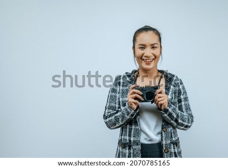 Portrait of Asian woman wearing casual clothes with a big smile on face,  holding a camera taking a picture. Isolated background in studio with blank space.