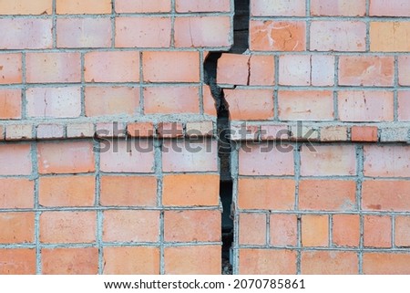 A huge (large) crack on the wall of a brick house.