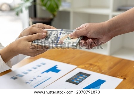 Picture of two people handing over a dollar, they are business partners who are doing corrupt behavior by bribing them for illegal mutual benefit. The concept of business fraud and bribery.