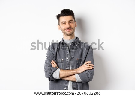 Proud handsome guy looking satisfied, cross arms on chest and smile at camera, checking out something good, standing on white background