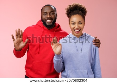 Happy african-american couple man woman hugging friendly guy embracing girl supportive together waving you greeting say hello smiling happily inviting come in welcoming, standing pink background