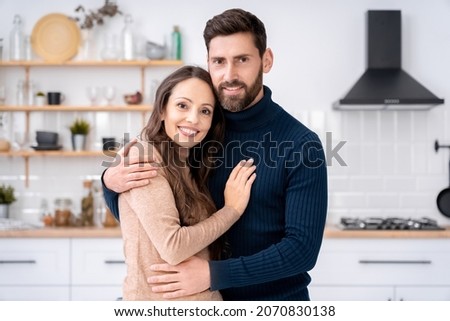Portrait of loving wife and husband hugging looking at camera posing together at home kitchen. Charming romantic couple showing love, adoration, devotion and care. Family bonding and relationship Royalty-Free Stock Photo #2070830138