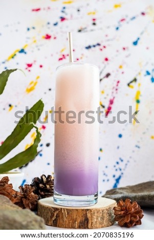 Minimalist Concept Idea. purple soda milk ice drink on stone with green leaves on abstract background.