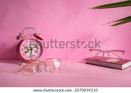 Product Presentation of Minimalist Concept Idea. glasses on book and alarm clock on pink background.