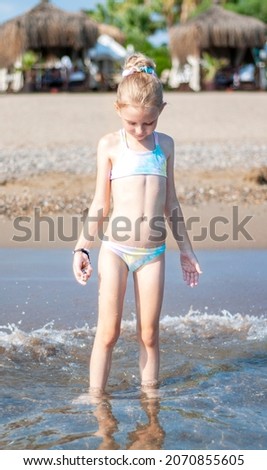 Little girl in a bathing suit playing on the beach by the sea