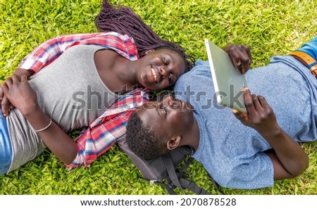 Afro american couple relaxing happy on the grass looking at tablet screen, downward view.