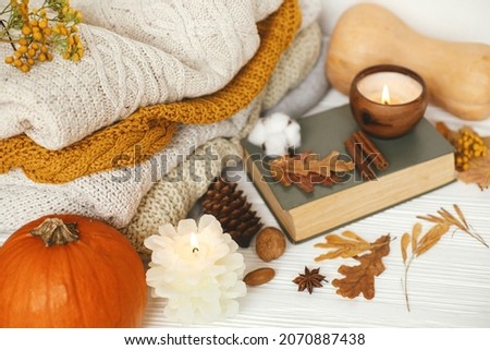 Cozy autumn days, slow living. Pumpkin, cozy sweaters, autumn leaves, burning candle and vintage book on white wooden background in room.Happy Thanksgiving