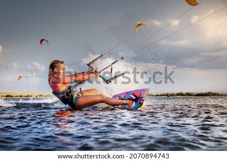Professional kitesurfer young caucasian woman glides on a board along the sea surface at sunset against the backdrop of beautiful clouds and other kites. Active water sports Royalty-Free Stock Photo #2070894743