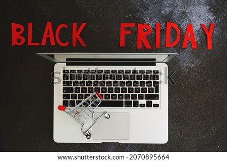 Black Friday concept. Inscription "black friday", laptop, mini shopping cart on black background. Copy space, top view, flat lay. Creative holiday flyer. Online sale and discounts