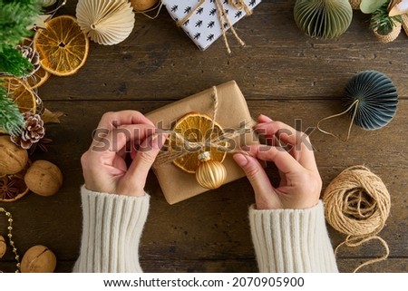 Unrecognizable female tying knot christmas gift in craft paper. New Year decor background. Wintertime handcraft. Preparation for celebration xmas. Family surprises Hand-on activity concept Royalty-Free Stock Photo #2070905900
