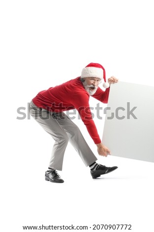Emotional mature man in Santa Claus hat and with blank poster on white background