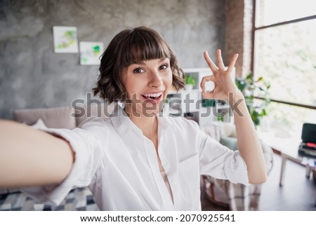 Self-portrait of attractive cheerful girl showing ok-sign having fun good solution at home loft brick interior indoors