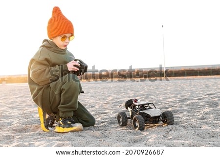 Boy kid playing radio control car riding on sand outdoor enjoying happy childhood Royalty-Free Stock Photo #2070926687
