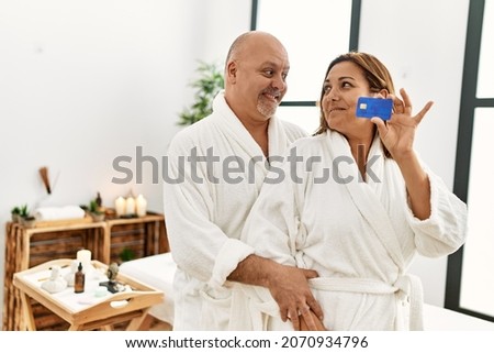 Middle age hispanic couple smiling happy and  holding credit card at beauty center.