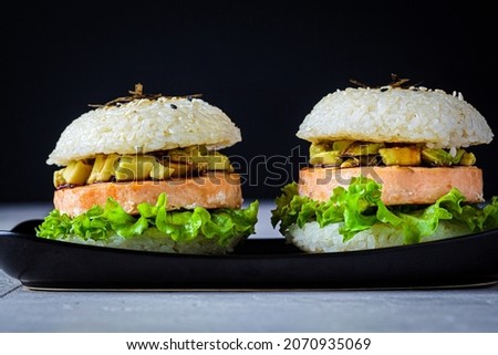 Rice burger with salmon cutlet, avocado and soy sauce, black background.