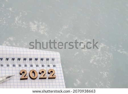 Notebook and pen on the grey. Wooden numbers date 2022. A blank sheet of paper and a white pen.