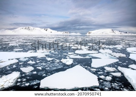 Floating ice in the Arctic sea, with the snow covered mountains of Svalbard on the horizon, a Norwegian archipelago between mainland Norway and the North Pole Royalty-Free Stock Photo #2070950741