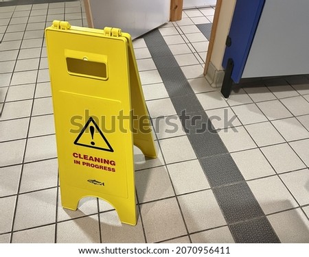 A yellow warning cleaning sign board on a tiled floor in the toilet