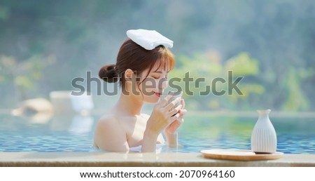 asian young woman is drinking sake while she relaxing sitting in hot spring with towel on head Royalty-Free Stock Photo #2070964160