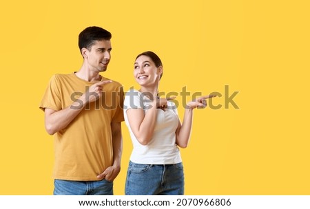 Young gossip couple pointing at something on yellow background