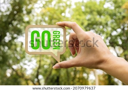 A woman's hand holds a sign inside which the inscription - Go Green. Ecology concept. Closeup of wooden speech buble with words Go Green.