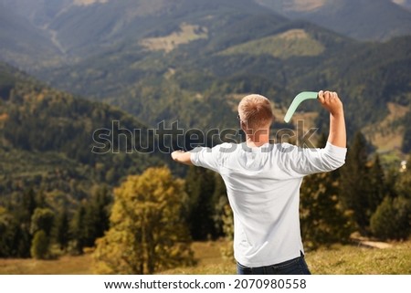 Man throwing boomerang in mountains on sunny day, back view. Space for text Royalty-Free Stock Photo #2070980558