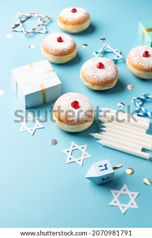 Hanukkah sweet doughnuts sufganiyot (traditional donuts) with fruit jelly jam, gift boxes, spinnig driedel and white candles on blue paper background. Jewish holiday Hanukkah concept, copy space.