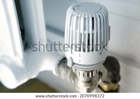 temperature regulation in the house with a thermostat on the white radiator, close-up valve, concept of saving heat, the beginning of the heating season, shallow depth of field focus Royalty-Free Stock Photo #2070998372