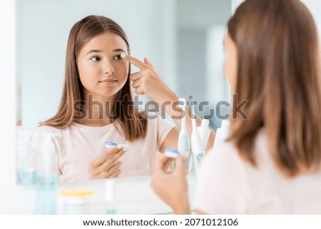 health, vision and old people concept - teenage girl applying contact lenses in front of mirror at home bathroom Royalty-Free Stock Photo #2071012106
