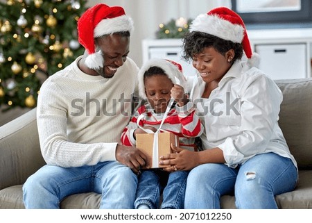 family, winter holidays and people concept - happy african american mother, father and little son opening gift box at home on christmas