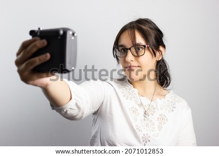 Young girl on a white background taking a selfie while smiling with an old camera.