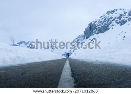 Photographer in the middle of a mountain road completely covered in snow.